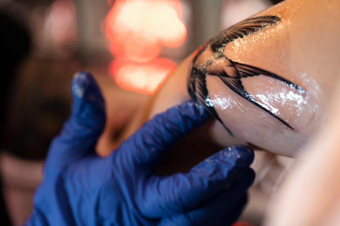 Artist applying ointment to a fresh tattoo with gloved hands